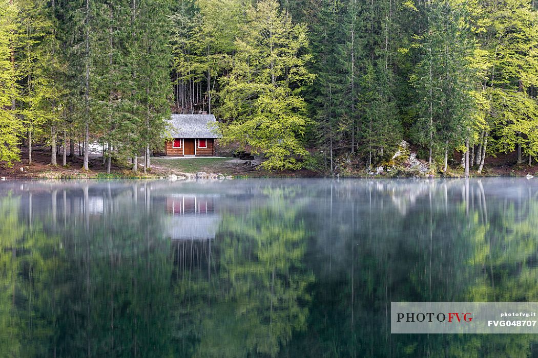 A small house reflects on the beautiful waters of the lower lake of Fusine, Tarvisio, Julian Alps, Friuli Venezia Giulia, Italy, Europe